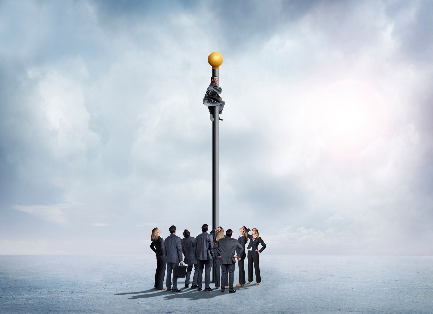 Group Of Business People Look Up At Businessman Clinging To A Tall Flagpole